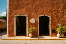 Bright Beautiful Building Wall Red Hot Orange Texture Shaby. Two Arched Entrances With Doors. Pots And Plants. Streets Of A Mexican City Valladolid