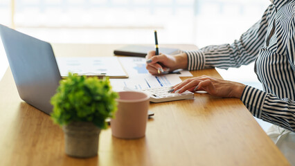 Close up a Business woman holding pen pointing to business chart paper for doing math finance on a wooden desk, tax, accounting, statistics concept.