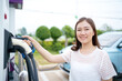 © DG PhotoStock - Happy Asian woman holding a DC - CCS type 2 EV charging connector at EV charging station.