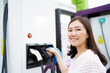 © DG PhotoStock - Happy Asian woman holding a DC - CCS type 2 EV charging connector at EV charging station.