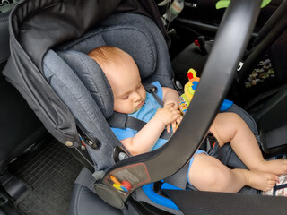 Cute baby boy sleeping in children care safety seat while riding