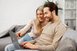 © Vadim Pastuh - Caucasian couple in love spending leisure time with laptop at home. Happy girlfriend and her boyfriend looking at the laptop screen while sitting on the sofa, watching movies