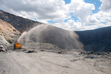 Wall Mural - Heavy truck pours the road with water in the iron ore quarry. Dust removal, protection of the environment. Irrigation of the road from dust