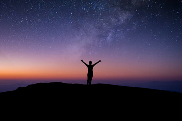 Wall Mural - Silhouette of young woman traveler and backpacker watched the star and milky way alone on top of the mountain. She open arms and enjoyed traveling and was successful when he reached the summit.