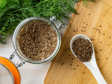 Organic Dill Seeds In A Glass Jar And White Spoon Over Kitchen Table. Cooking With Natural Spices, Seasonings And Condiments. Whole Anethum Graveolens Fruits For Herbal Medicine.