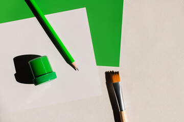 Poster - top view of paintbrush, pencil and jar with paint near white and green papers on textured background.