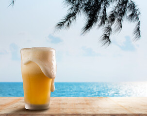 a beer bubble overflowing from a glass of beer lay on a wooden counter by the beach overlooking the sea and sky.