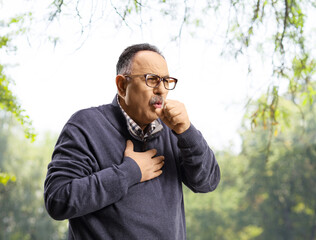 Mature man in a park caughing and holding his chest