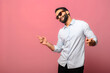© Vadim Pastuh - Overjoyed Indian man wearing sunglasses dancing, makes movements to music, smiles positively, being in high spirit. Carefree hispanic guy in blue jeans shirt dances isolated on pink