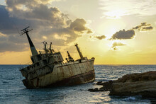 A Large Rusty Shipwreck On A Rocky Coast Against A Beautiful Sunset Background