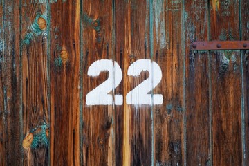 White colour number twenty two on an old abandoned weathered painted natural rusty brown wooden gate of a garage in Budapest suburb, Hungary