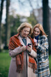 A grandmother is browsing her phone during a walk in the park with her adolescent granddaughter in cold weather.