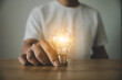 © Monster Ztudio - Hand holding light bulb on wood table. Concept of inspiration creative idea thinking and future technology innovation