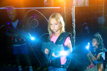 Canvas Print - Positive little girl aiming laser gun at other players during lasertag game in dark room