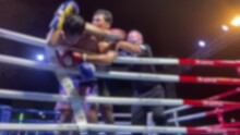 Blurred Motion Background Youth Amateur Muay Thai Boxing Match Kick Punch Knee And Elbow Attack. Thai Boxing Fighting On Stage Ringside View At Night Time Outdoor Arena Spotlight