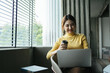 © PaeGAG - Portrait of beautiful Asian woman sitting indoors at coffee shop restaurant during summer, using smart wireless technology computer laptop and smartphone, relaxing coffee break at cafe restaurant.