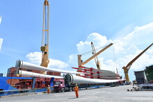 Large Wind Turbine Rotor Blades Being Unloaded From A Ship Onto A Telescopic Trailer For Onward Transportation By Road To The Construction Site