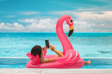 Summer Swimming Pool Vacation Relaxing Woman Floating In Flamingo Inflatable Float Using Mobile Phone At Luxury Resort Sunbathing. Caribbean Travel Vacation Hotel Lifestyle