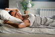 © NDABCREATIVITY - Happy girl waking up stretching arms on the bed in the morning