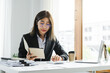 © Phushutter - Portrait of a short-haired Asian businesswoman using a notebook with a calculator to calculate accounting taxes in a modern office.