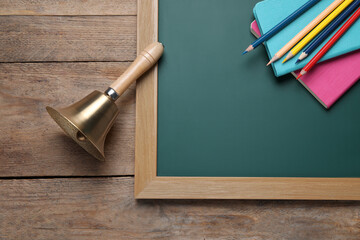 Wall Mural - Golden bell, green chalkboard and stationery on wooden background, flat lay. School days