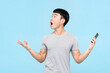 Astonished Asian man with mobile phone in hands looking up while standing on light blue isolated background in studio