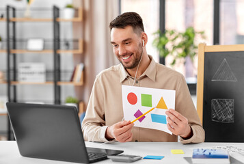 Sticker - distance education, primary school and remote job concept - happy smiling male teacher with laptop and picture of geometric shapes in different colors having online class at home office