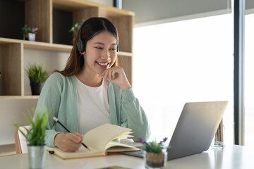 Wall Mural - Concentrate asian gial freelancer wearing headset, communicating with client via video computer call. Millennial pleasant professional female tutor giving online language class.