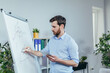 © Liubomir - Young businessman writing on white board with marker business strategy plan, man working in modern bright office