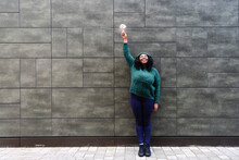 Smiling Woman Looking Up Holding Light Bulb In Front Of Gray Wall