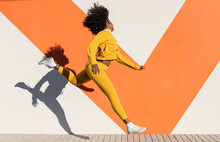 Young Woman Jumping By Wall On Footpath