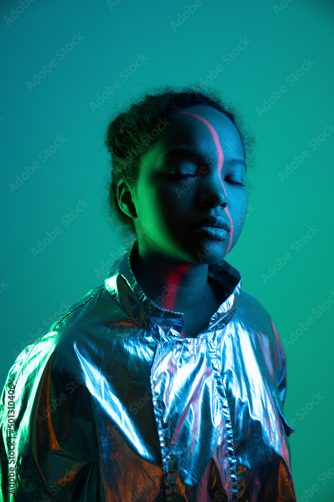 Laser light falling on woman's face standing with eyes closed against green background