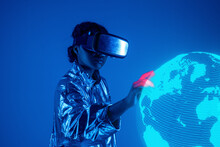 Woman Wearing Virtual Reality Simulator Touching Earth On Screen Against Blue Background