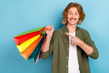 Poster - Portrait of attractive funky cheerful guy holding demonstrating bags offer order isolated over pastel blue color background