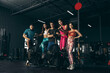 © master1305 - Group of young friends doing sports, training at gym indoors. Woman training at exercise bike. Posing