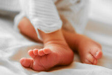Close-up Of Cute Sleeping Newborn Baby Feet On White Blanket. Baby In A White Gender Neutral Romper On The Bed. Little Fingers, Heels. Sleeping Baby, New Life, Cozy Home