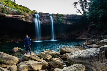 young man with waterfall streams falling from mountain top at morning long exposure shot