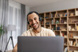 © Prostock-studio - Cheerful middle eastern guy having video chat via laptop wearing wireless headphones, looking at screen and smiling