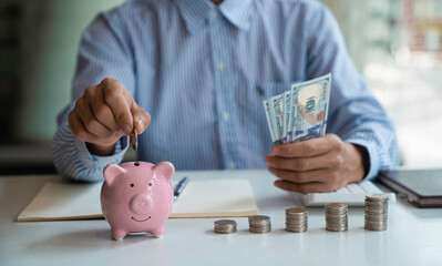 Wall Mural - Businessman with a coin in a piggy bank along with pressing the calculator and writing down savings for the future after retirement, ideas for saving money for the future and life after retirement