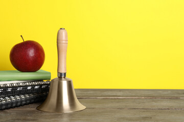 Wall Mural - Golden school bell, apple and notebooks on wooden table against yellow background, space for text
