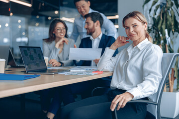 Wall Mural - Smiling confident businesswoman sitting on meeting in office with her colleagues at background. Business concept