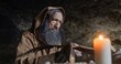 © procinemastock - Elderly monk taking notes with quill in cave