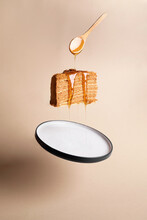 Vertical shot of a slice of honey cake in the air with a spoon of honey pouring on it