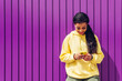 © Dani D.G - Young woman of african-american ethnicity using her smatphone on purple background. Influencer girl with yellow clothes using her mobile phone and her social networks.
