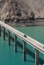 Vertical Aerial Drone Shot Of A Bridge On The Teal Water At Feet Of Hills With Cars Driving Across