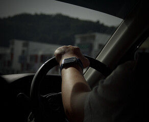 Sticker - Back shot of a male with a watch driving a car holding the wheel with gray green mountains outside