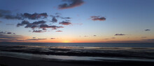 Wide Panoramic Twilight Beach Scene With Darkening Pink Sunset Sky And Clouds Reflected In A Calm Sea And Water On The Beach