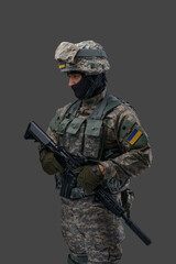 Wall Mural - Portrait of soldier from ukraine with rifle dressed in uniform looking away isolated on gray background.