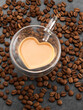 Glass cup in form of heart with coffee on coffee beans background.