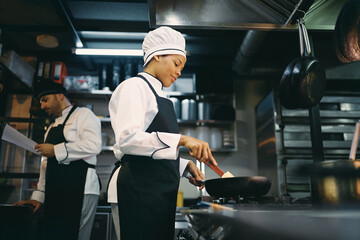 Wall Mural - Below view of black female chef preparing food in the kitchen.